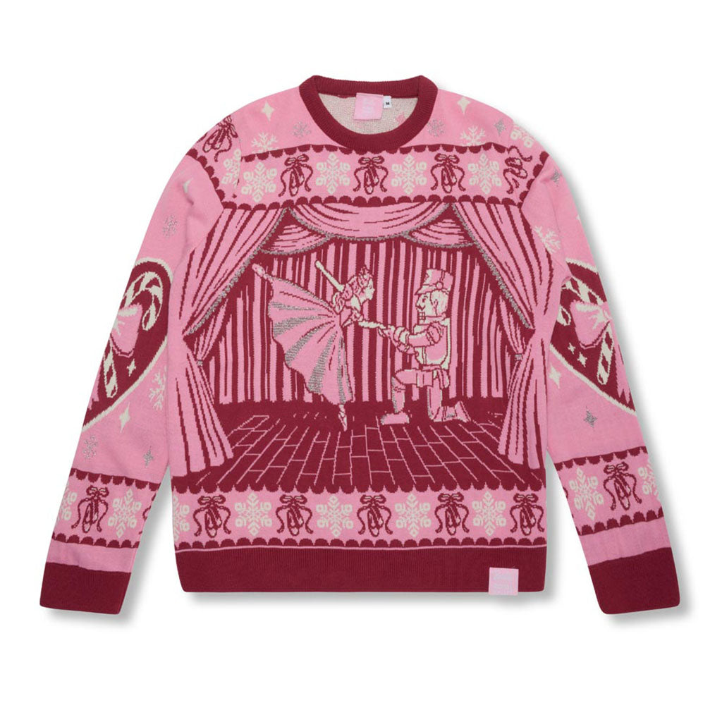 A pink and dark red Christmas Jumper featuring a central illustration of Clara and the Nutcracker on stage with curtains, with decorative patterns on the sleeves and hem.