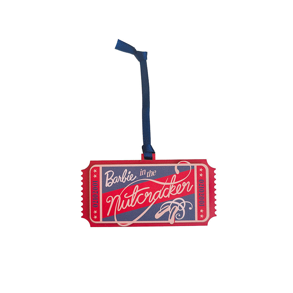 A Barbie-themed nutcracker decoration shaped like a ticket, featuring red, navy blue, and white lettering 'Barbie in the Nutcracker', with a dark blue hanging ribbon on a plain white background.