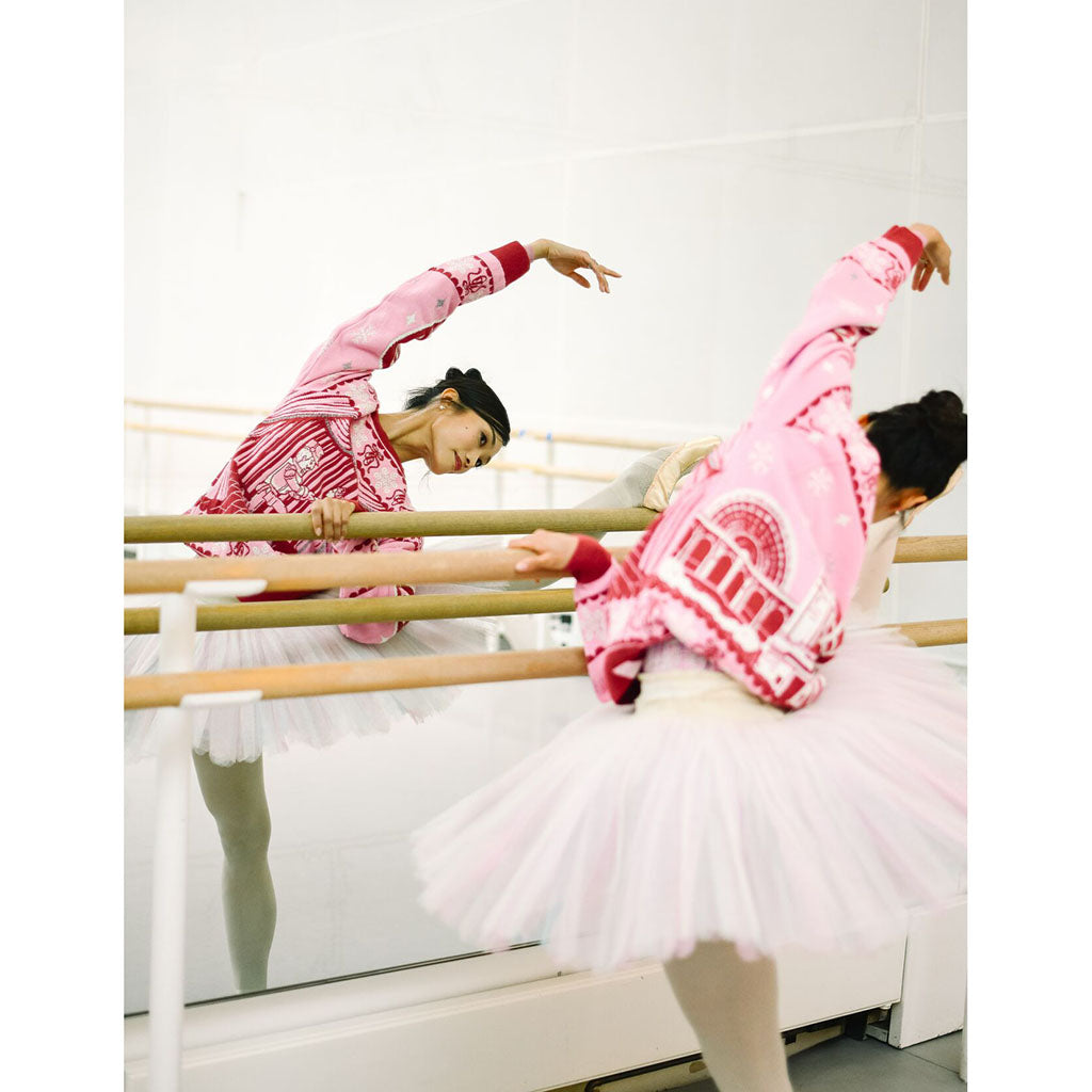 Principal dancer Fumi Kaneko practising in a pink Barbie Christmas Jumper and white tutu practicing at a ballet barre in a bright studio, with her reflected in the mirror.
