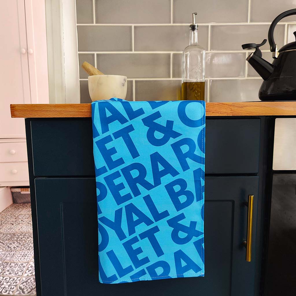 Blue signature tea towel with text hanging on a kitchen cabinet