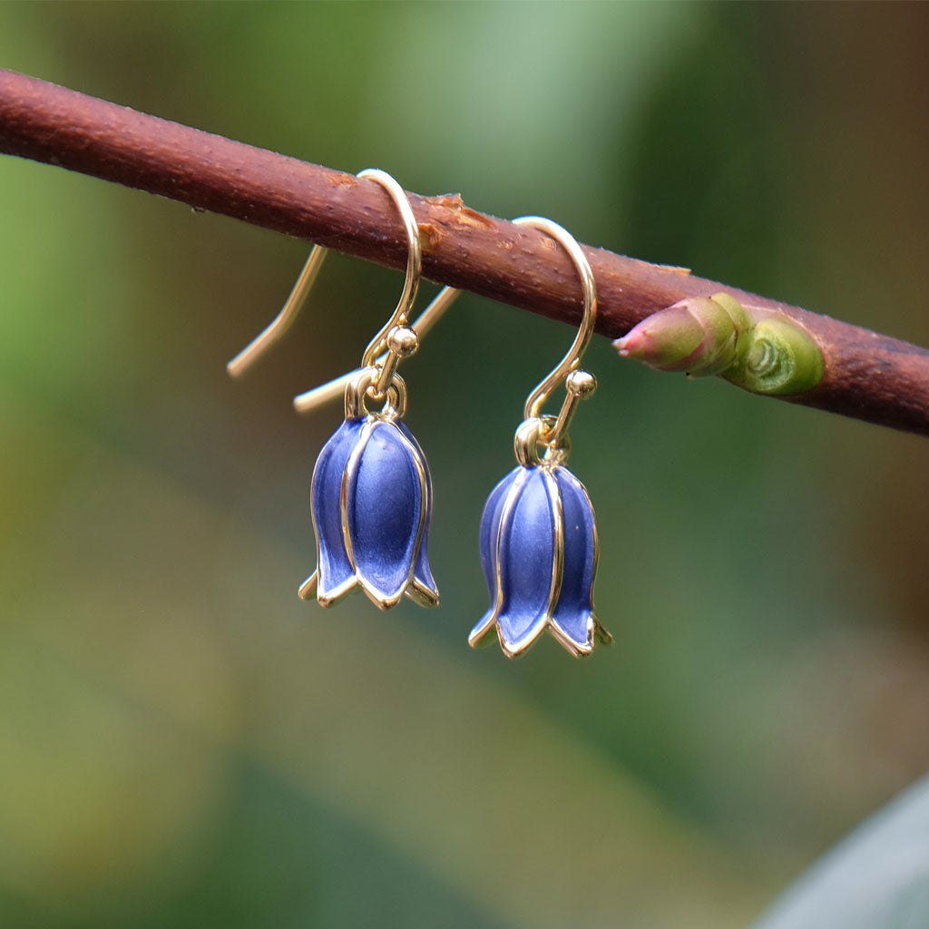 Bluebell-shaped earrings hanging on a branch with a blurred natural background