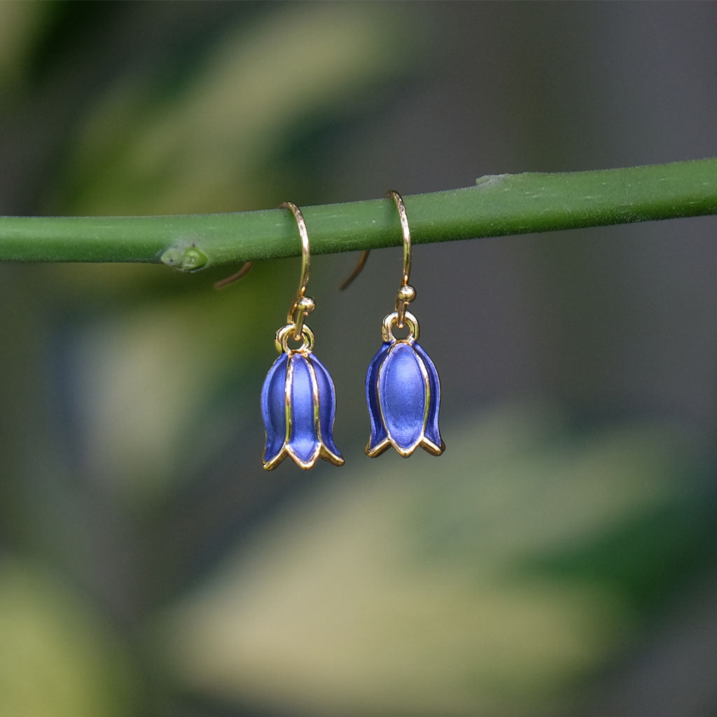 Blue flower-shaped earrings on a green stem with a blurred natural background