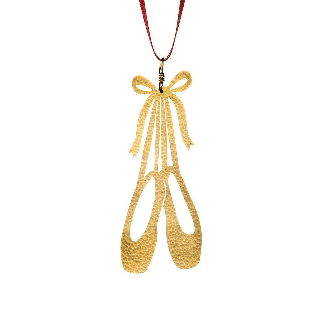 A brass decoration of a pair of ballet pointe shoes hanging by their ribbon on w white background
