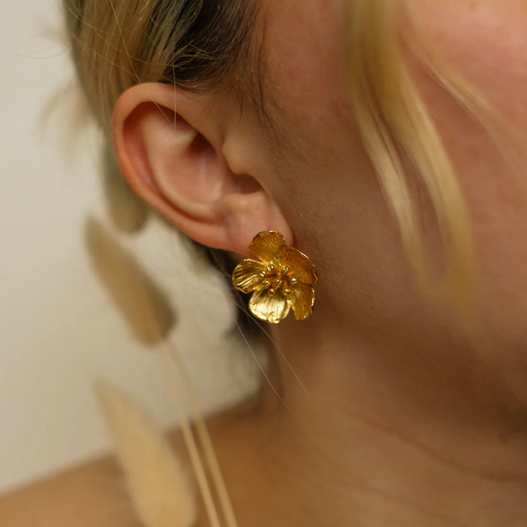 Close-up of a person wearing a gold buttercup earring.