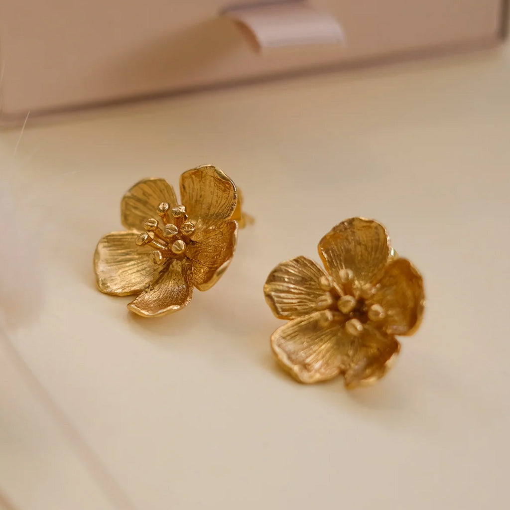 Pair of gold flower-shaped buttercup earrings on a white background