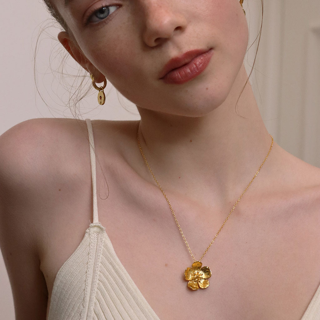 Woman wearing a gold plated brass necklace with a floral pendant against a neutral background
