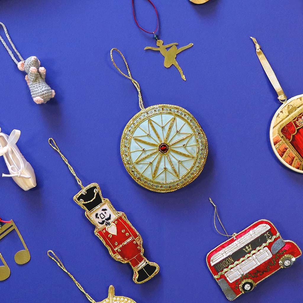 Decorative circular decoration inspired by the auditorium ceiling  at the RBO with gold  and blue detailing and a red gemstone on a white background