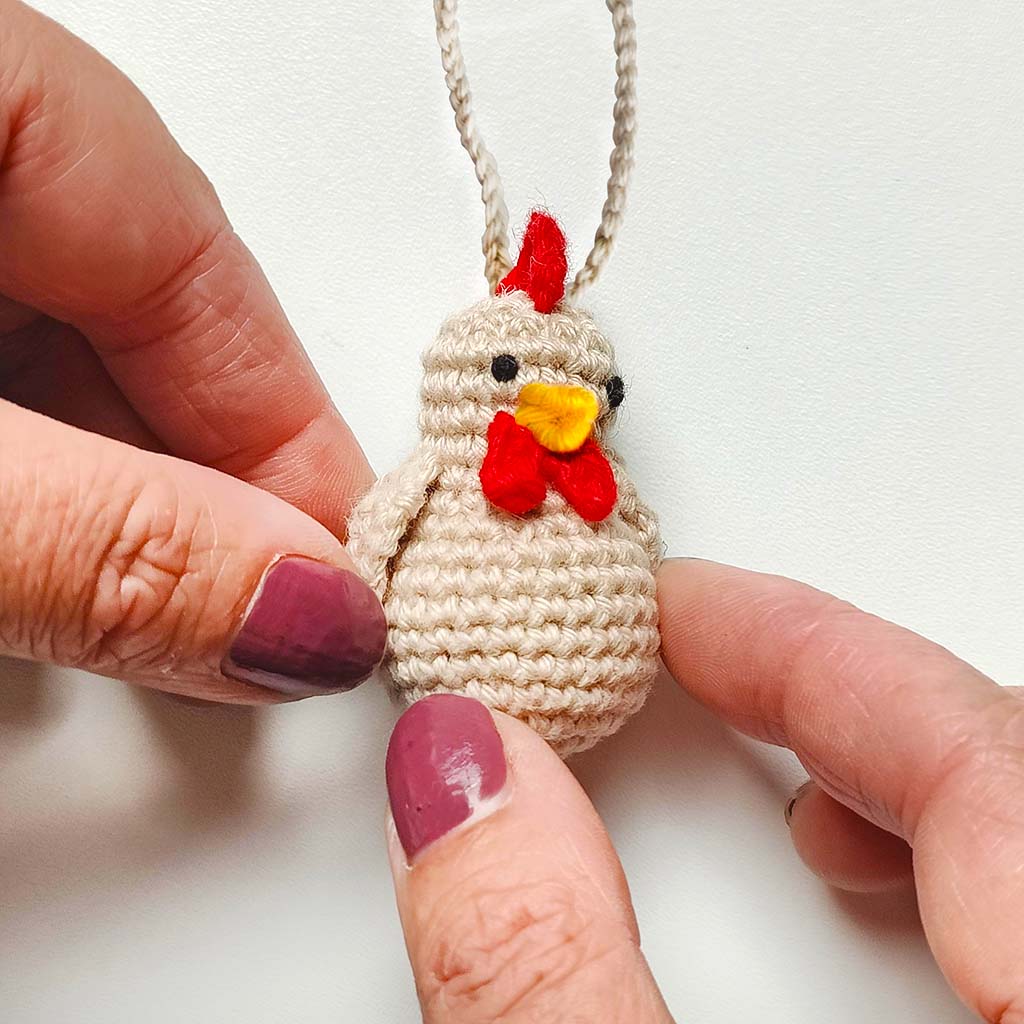 Crocheted chicken decoration with a red bow and yellow beak on a white background