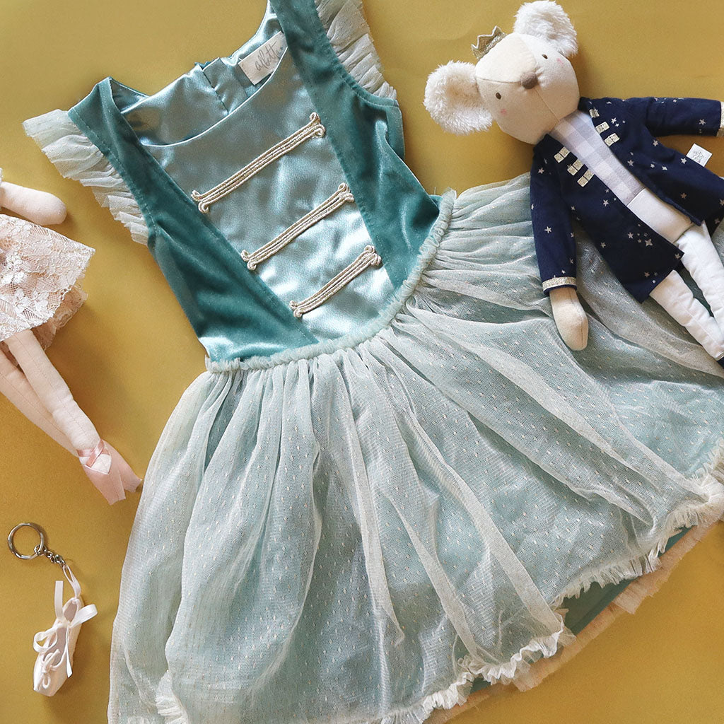 Children&#39;s nutcracker ballet dress with teal bodice and white skirt on a yellow background, accompanied by a mouse king doll and ballet shoe keyring.