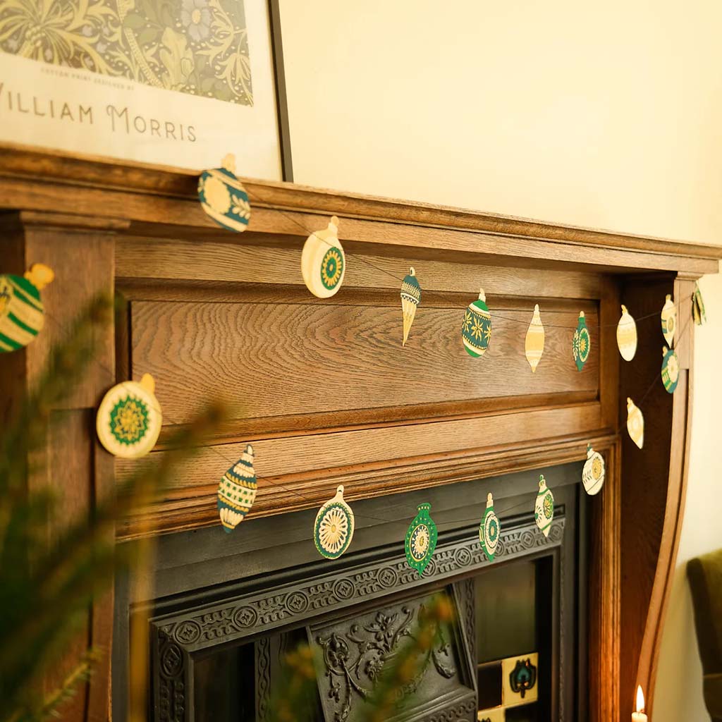 Decorative garland made of string with green and gold paper ornaments hanging above a fireplace.