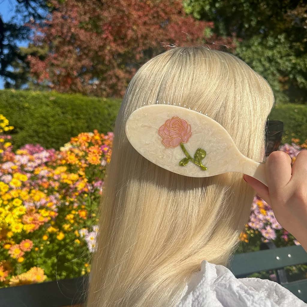 model with blonde hair using the cream brush in a garden with flowers in the background