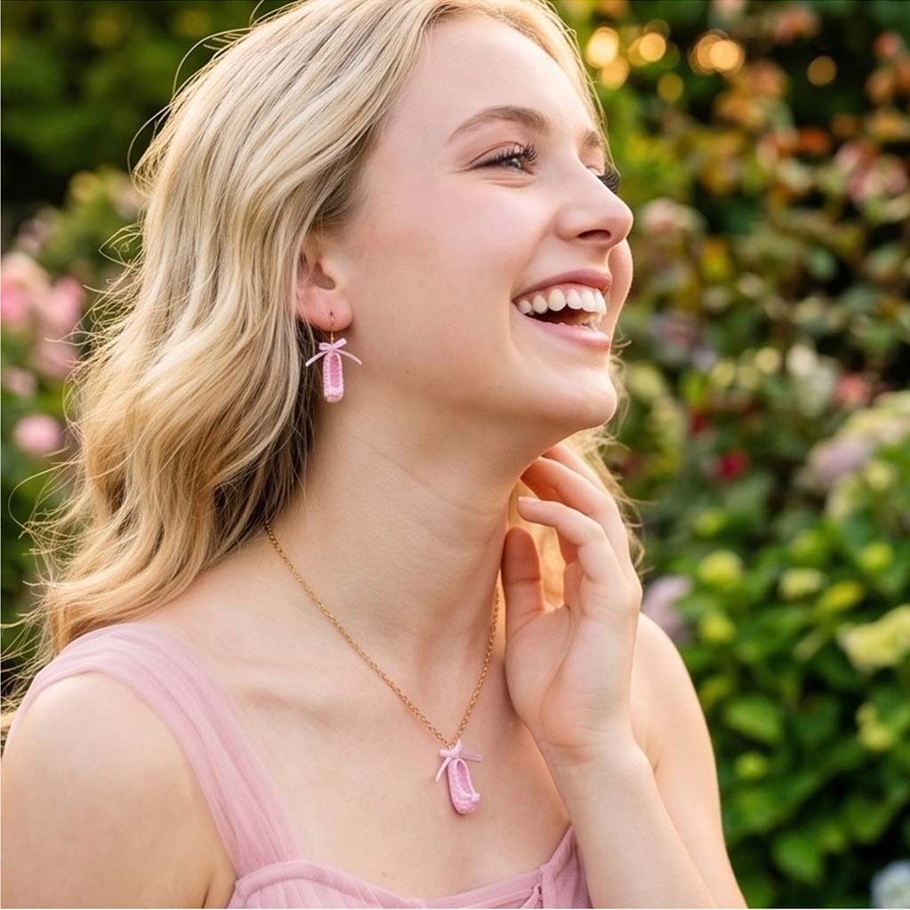 Woman wearing pink crochet ballet shoe earrings and a necklace with a blurred green background