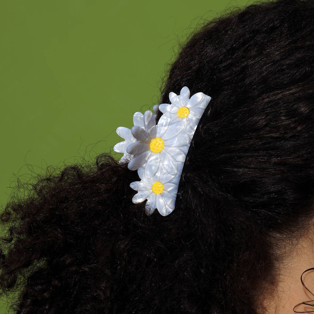 Daisy flowers clip with white flowers and yellow centers on a person's hair against a green background