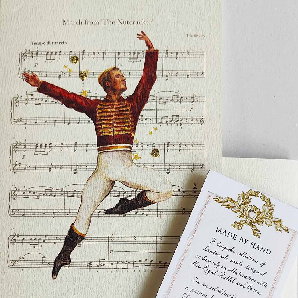 A close up of a greeting card featuring a Nutcracker dancer in a red and gold striped jacket and white pants leaping over musical notation, with the text 'March from The Nutcracker' at the top.