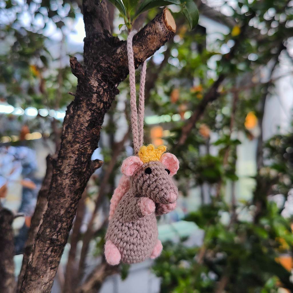 Crocheted mouse ornament with a yellow crown hanging from a tree branch.