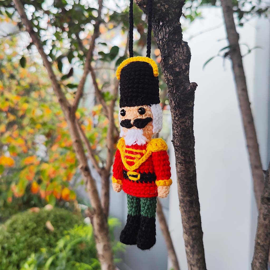 Crocheted nutcracker with a red jacket and black hat on a white background