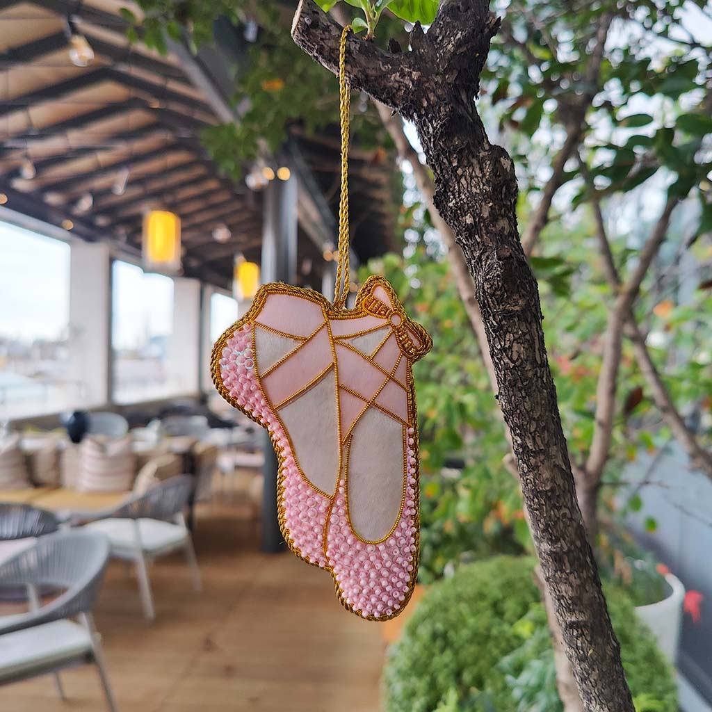 a pink beaded ballet shoe decoration  with gold trim on a white background