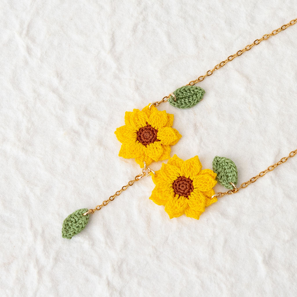 Two crochet sunflower pendants on a gold necklace on a white background