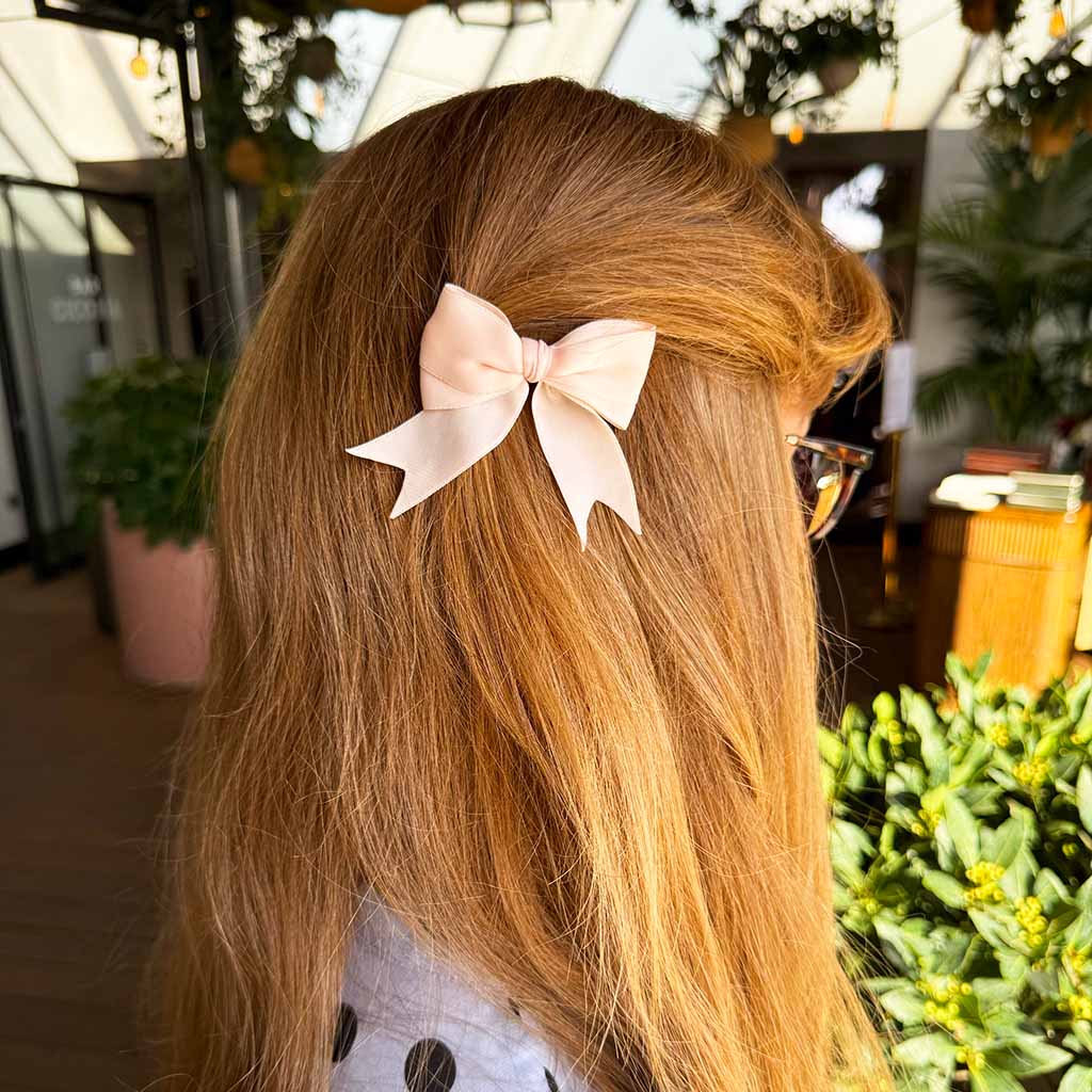 A pale blush pink satin ballet bow hairclip with two long ribbon tails, photographed against a solid white background.