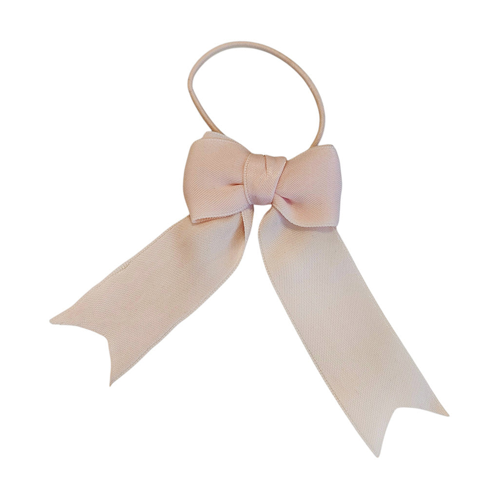 A light pink beige hair tie featuring a satin ribbon bow with two ribbon tails, shown on a plain white background made from recycled pointe shoes.