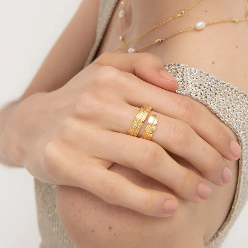 A close-up of a person's hand wearing a gold ring, one with a textured feather-like pattern.