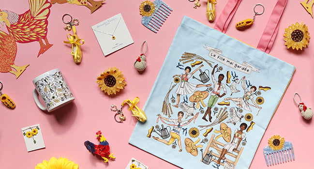 selection of ballet themed products on a pink background, including a tote, keyrings, mug, comb, jewellery, hair accessories and chicken garland