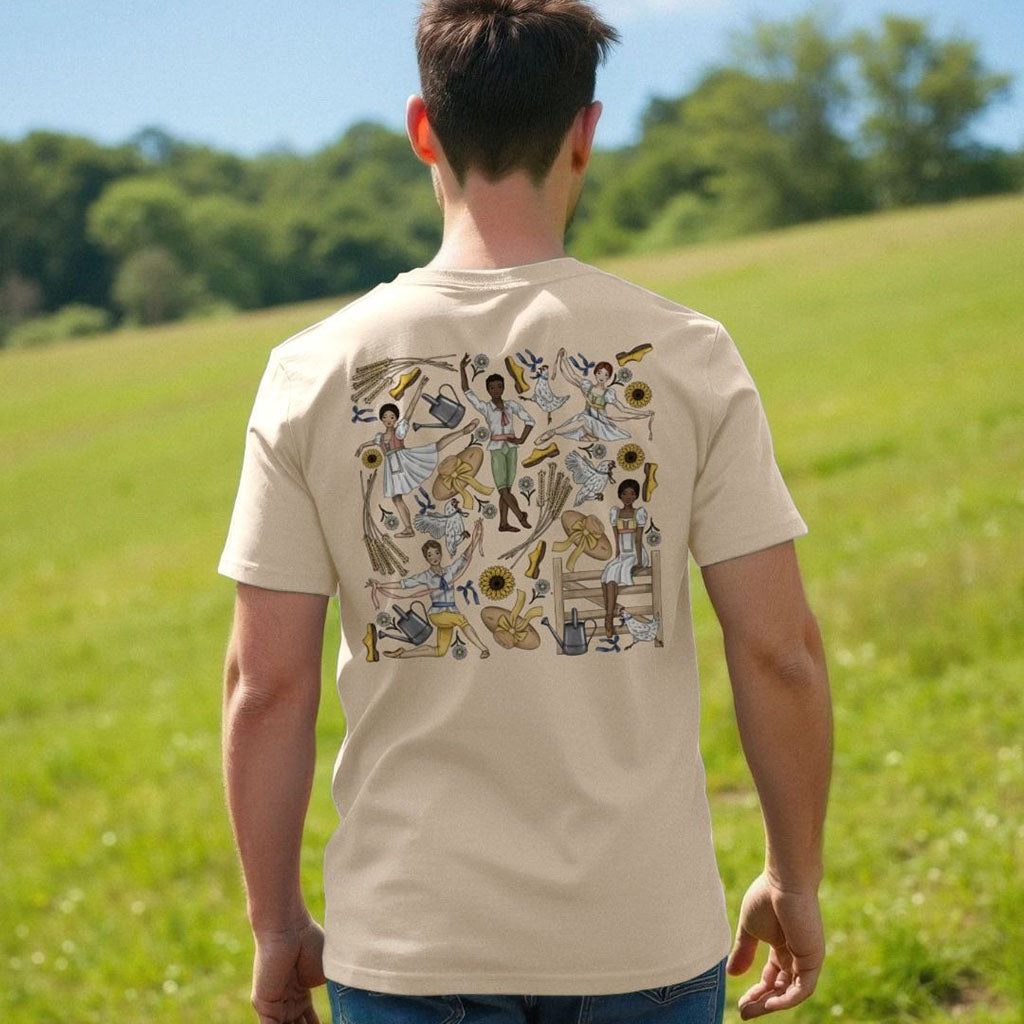 Person wearing a beige t-shirt with a colourful ballet illustration on the back, standing in a grassy field.