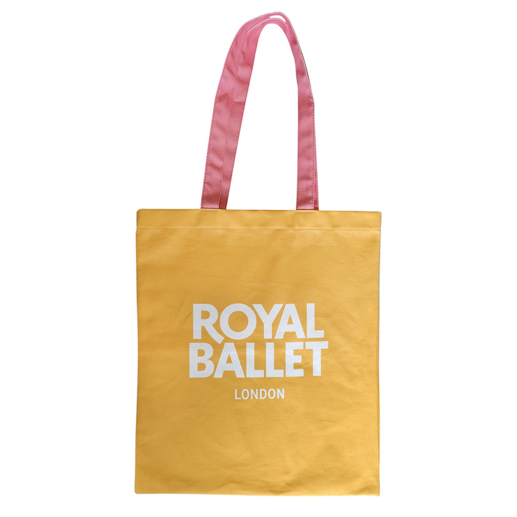 Back view of La Fille mal gardee tote, yellow with white text ROYAL BALLET LONDON with pink handles on a white background