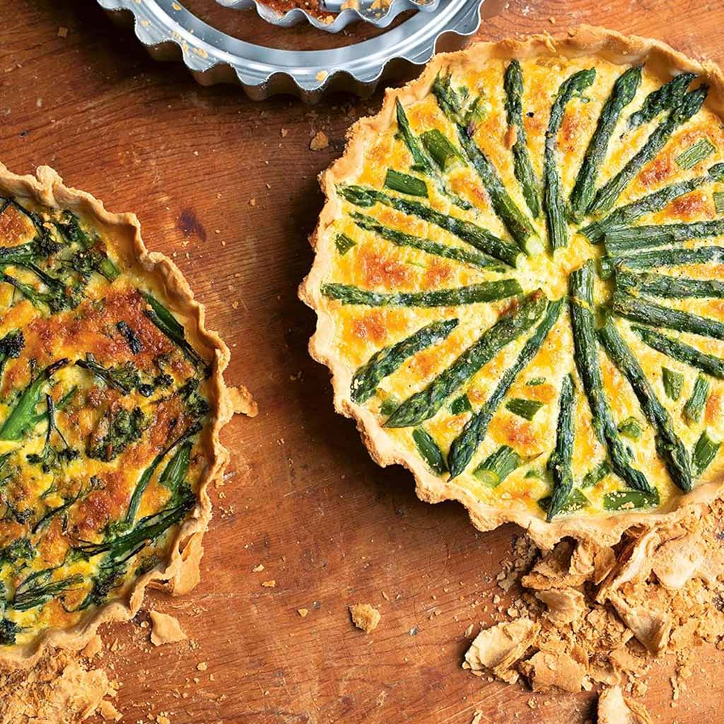Two small asparagus tarts on a wooden surface