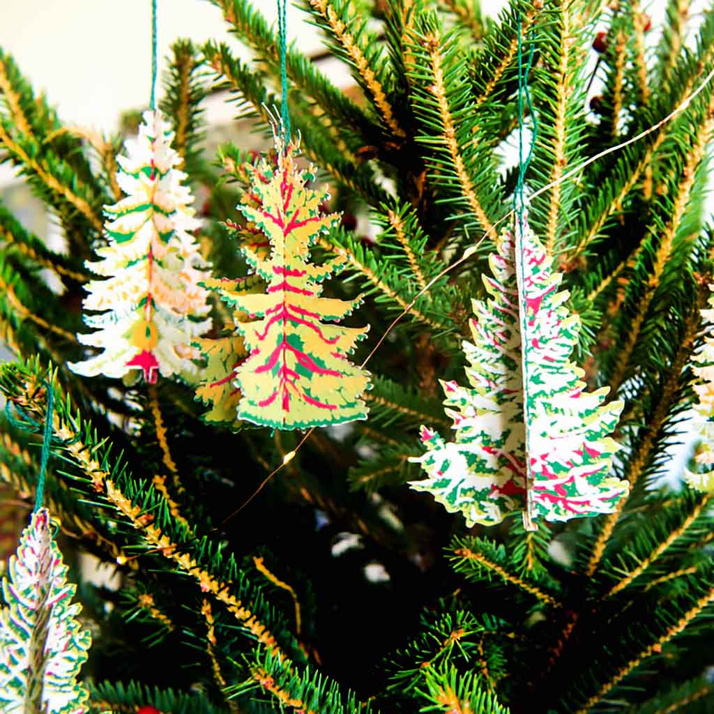 Decorative paper Christmas tree ornaments hanging on a green Christmas tree.