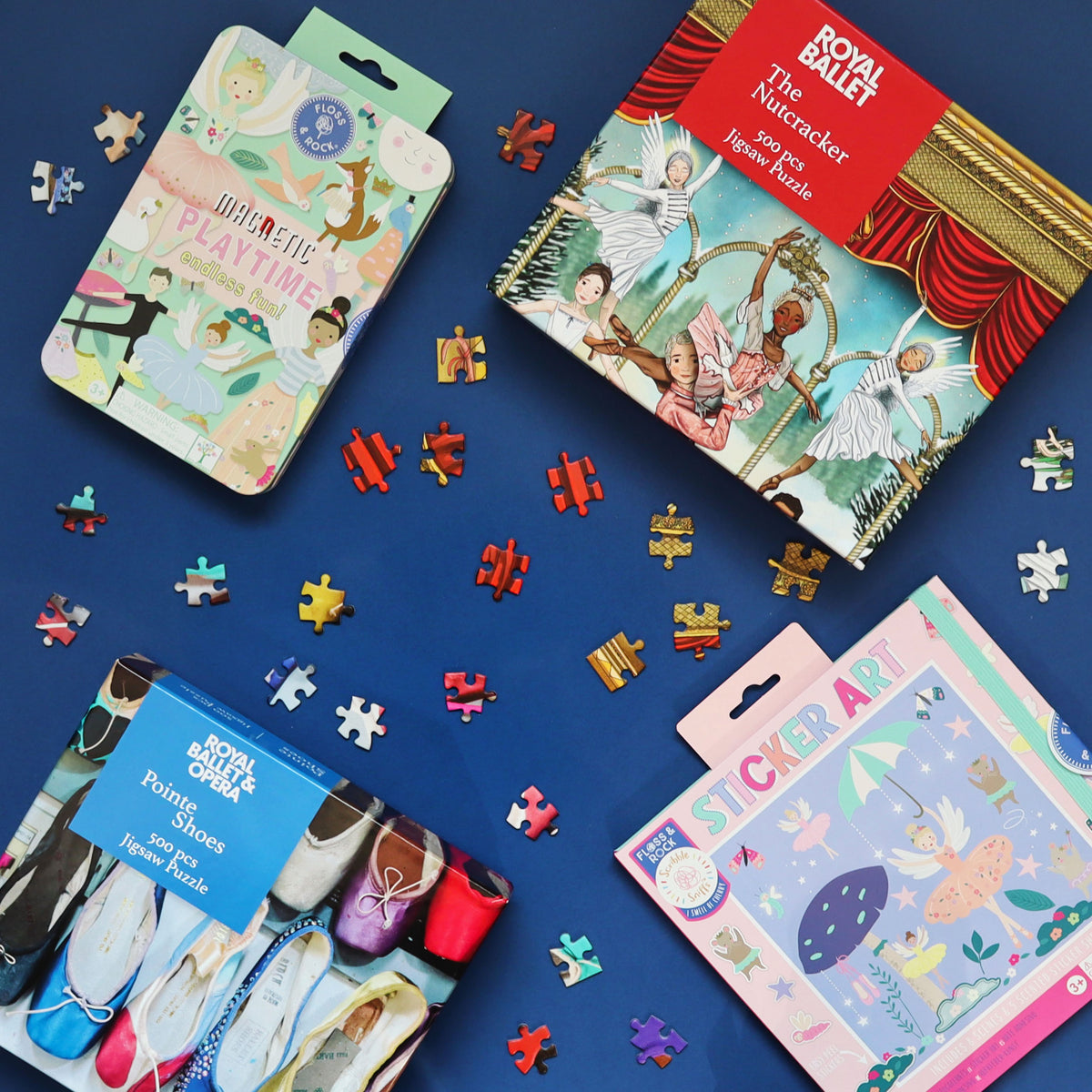 flat lay on a blue background of two jigsaws one for The Nutcracker and one with dyed pointe shoes, a magnetic playtime games tin and sticker art pack