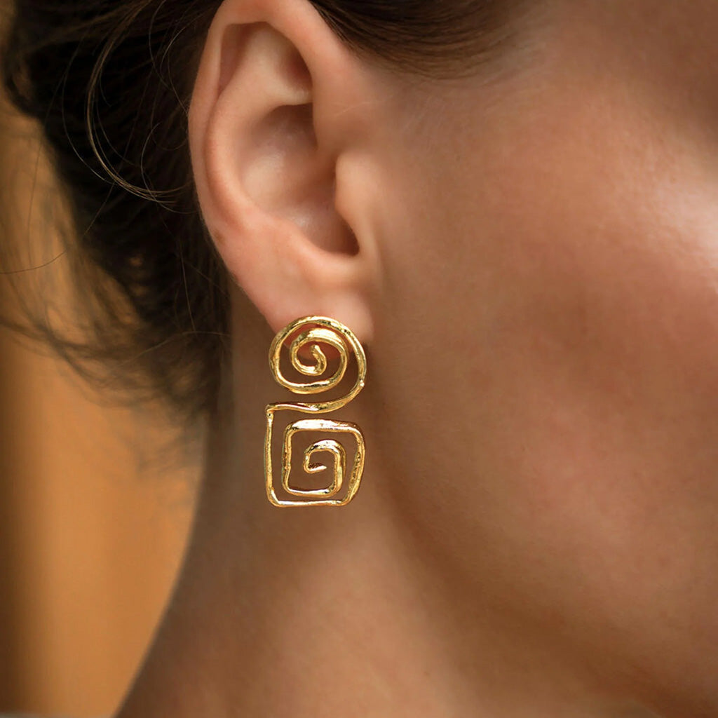 Gold spiral earrings worn by a person with a blurred background