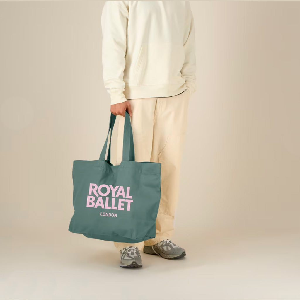 model holding green shopper bag with pink text 'Royal Ballet London' on a cream background
