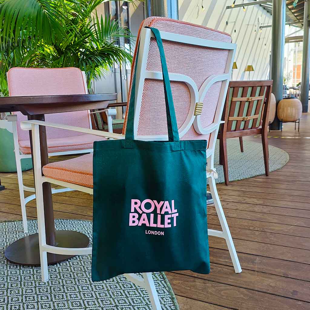 Green tote bag with 'Royal Ballet London' text on a chair in an outdoor setting.