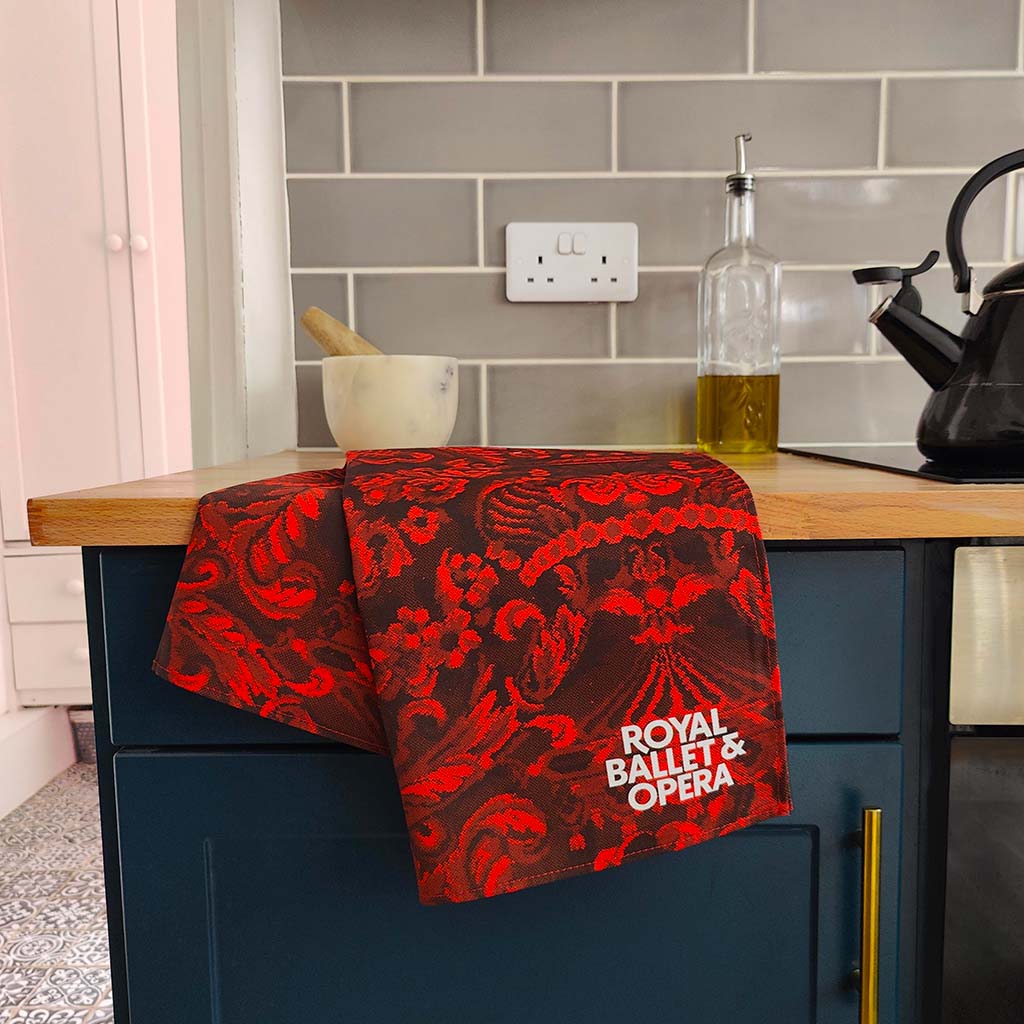 Red and black RBO carpet patterned tea towel with 'Royal Ballet & Opera' branding on a white background