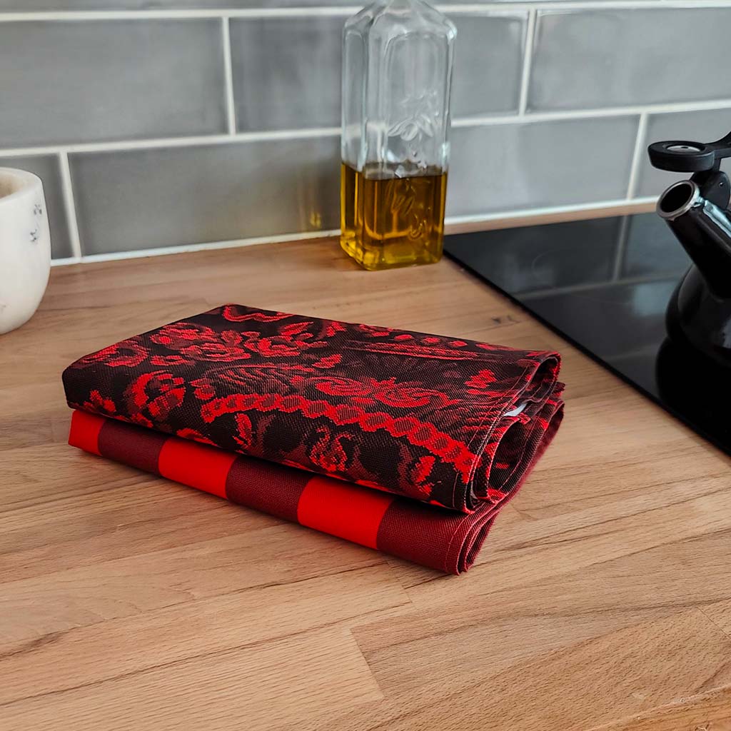 Red and black patterned tea towel on a wooden kitchen counter with a glass container of oil in the background.