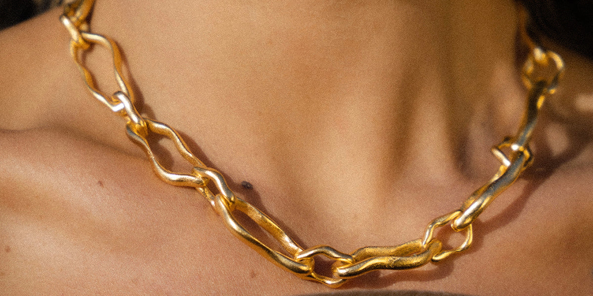 A close-up of a chunky, wavy Etta gold chain necklace worn on a person's neck and upper chest.