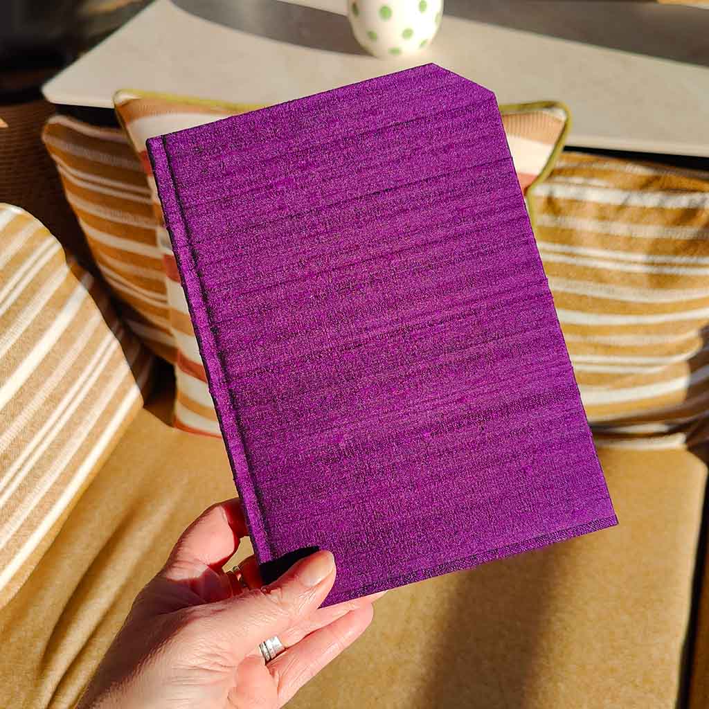 hand holding purple costume fabric notebook in front of a chair with yellow striped cushions