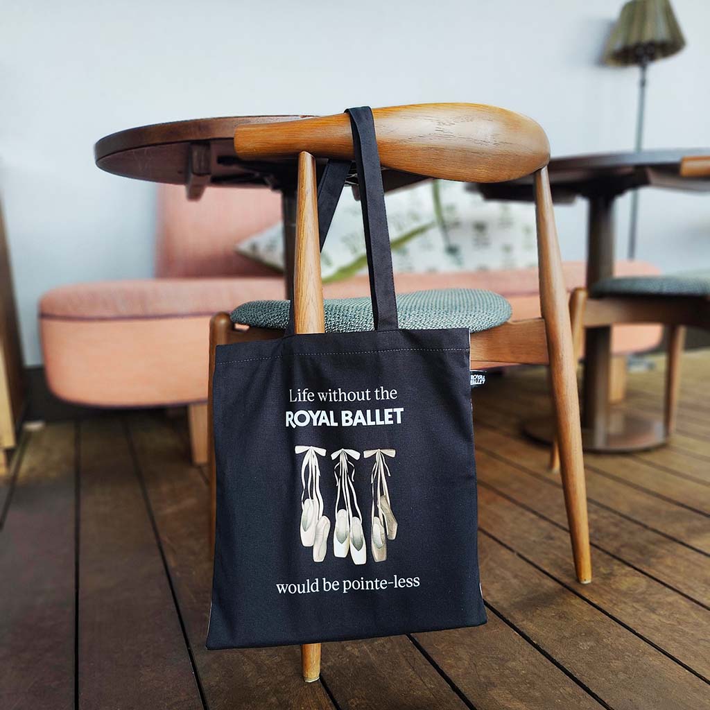 Black tote bag with ballet-themed design and text 'Life without the Royal Ballet would be pointe-less' hanging on a wooded chair