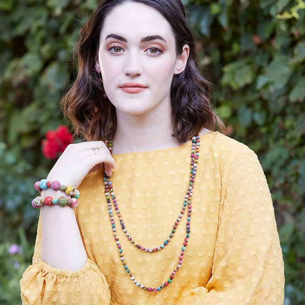 model in yellow wearing Kantha Bead Long Necklace and bracelets in front of greenery