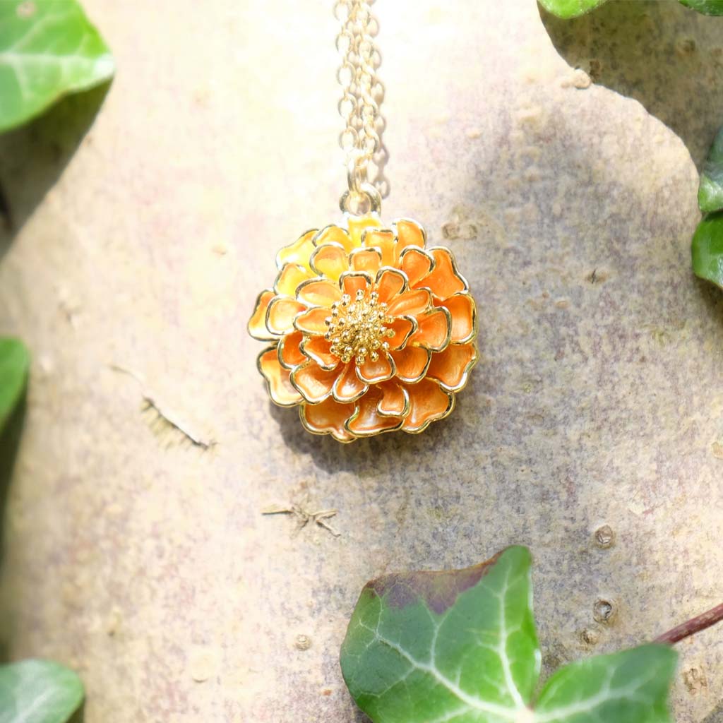 Gold flower-shaped pendant necklace on a stone background with green leaves.