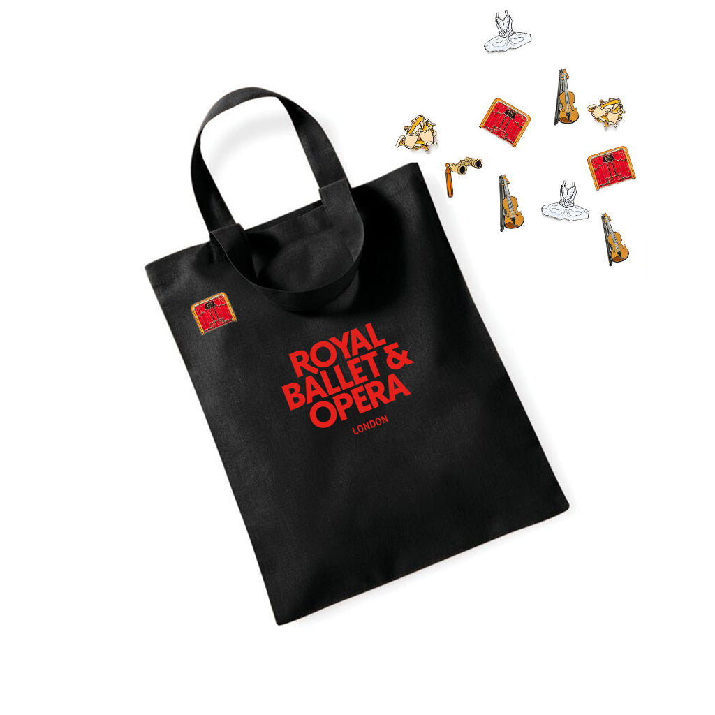 Small black tote bag with &#39;Royal Ballet &amp; Opera London&#39; text, surrounded by decorative pins on a white background