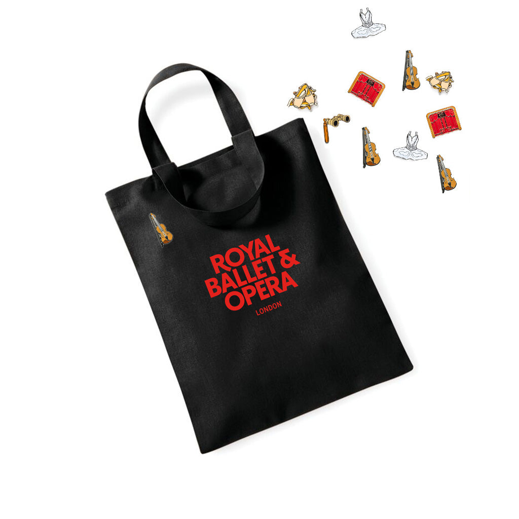 Violin pin badge on a small black tote bag with &#39;Royal Ballet &amp; Opera London&#39; text, with an assortment of other pin badges on a white  background.