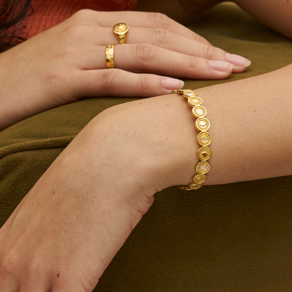 Gold bracelet and rings on a person&#39;s wrist and hand against a brown background