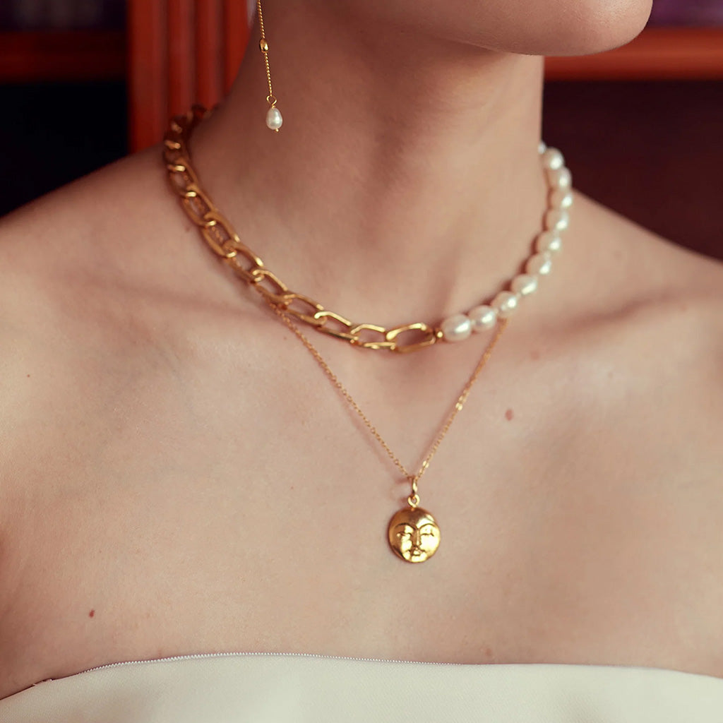 Gold necklace with a face pendant on a white background