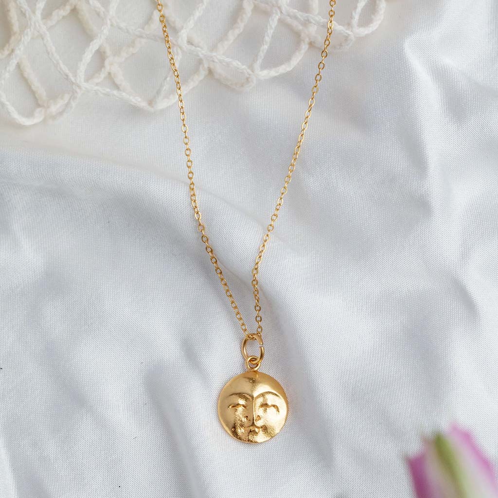 Gold necklace with a face pendant on a white fabric background