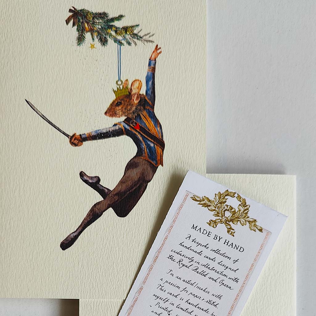 A greeting card featuring a whimsical illustration of a mouse dressed in a blue and gold uniform with a crown, leaping while holding a sword and a decorated fur tree branch, set against a textured off-white background.