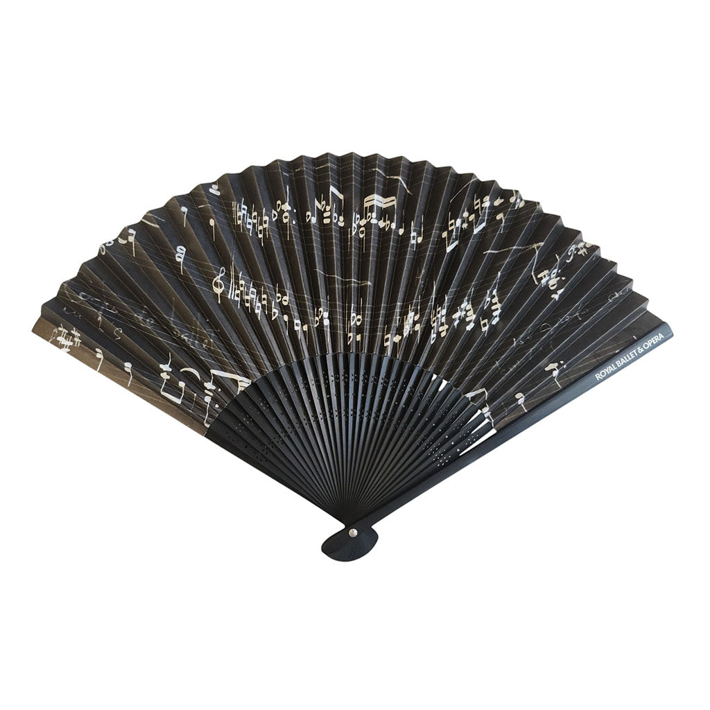 A black folding hand fan with a printed pattern of white musical notes and symbols, shown open against a plain white background.