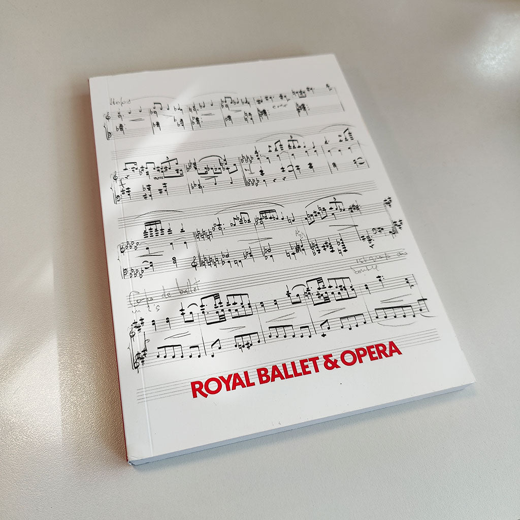A softcover A5 notebook with red text Royal Ballet &amp; Opera, featuring a white background with black musical notation and the title in red text at the bottom on a grey shadow bckground