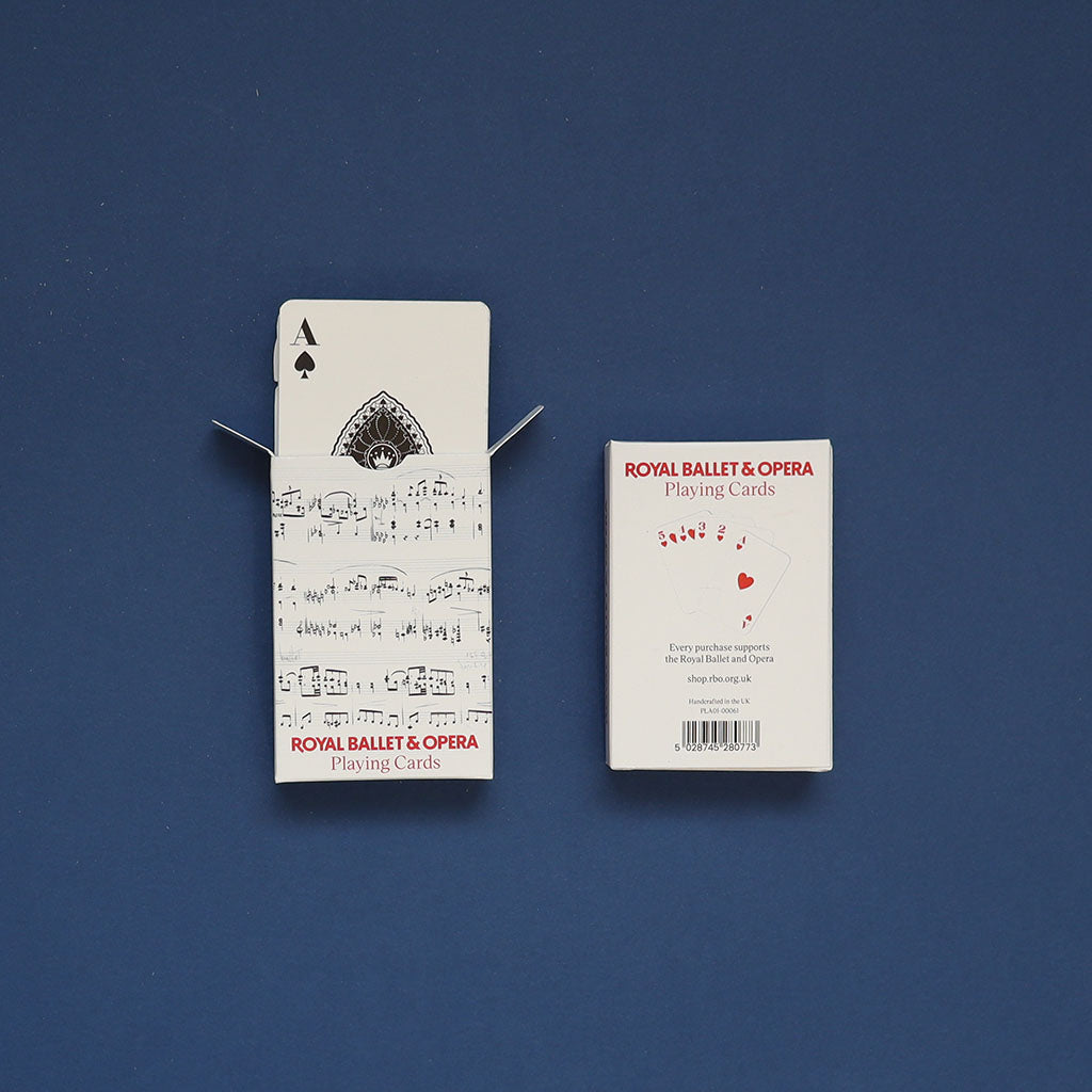 A deck of Royal Ballet &amp; Opera themed playing cards shown with its packaging on a dark blue background. The left side displays the back of an Ace of Spades card with musical notation, and the right side shows the white product box with red text.